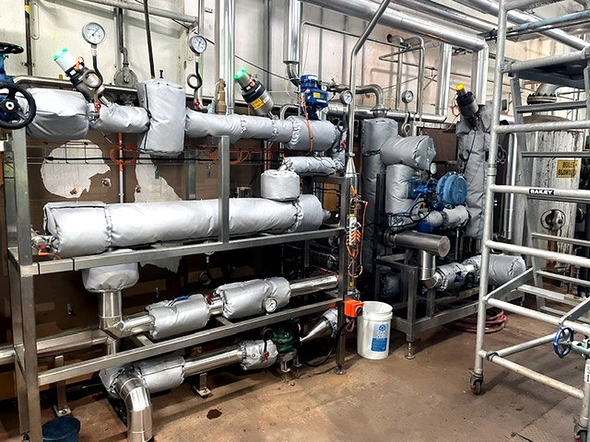 Dense industrial process area with thermal jackets across multiple levels of pipe manifolds